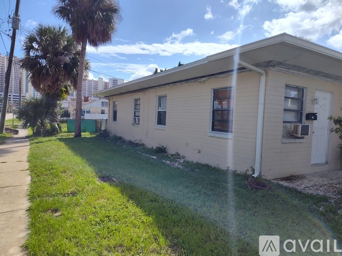A house with a white door and windows is surrounded by a grassy area and a sidewalk.