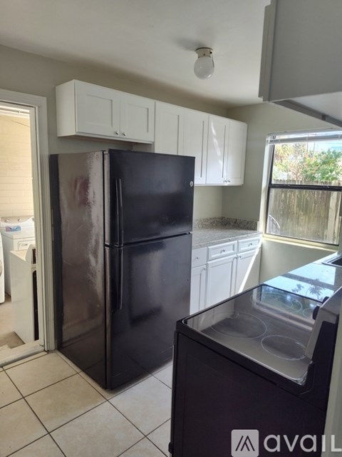 A black fridge in a kitchen with white cabinets.