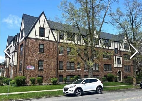 A white car is parked in front of a brick building with a black roof.