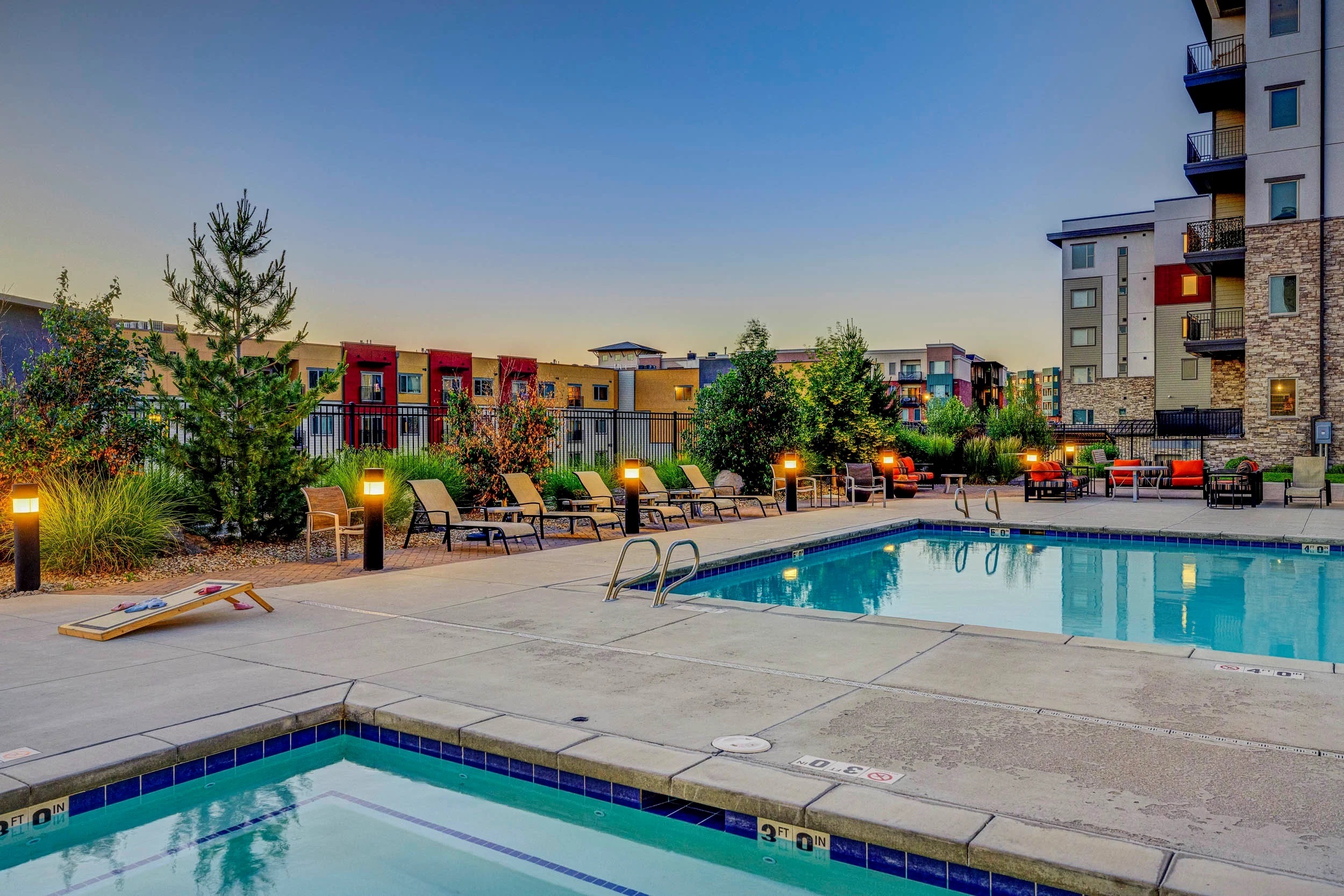 A pool surrounded by chairs and trees with buildings in the background.