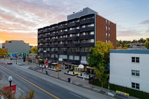 A large building with a balcony on the second floor is in the middle of a street.
