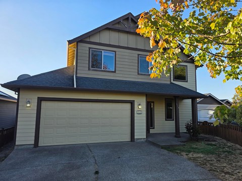 A house with a garage and a tree with yellow leaves in front.