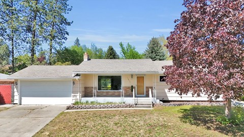 A house with a red garage door is surrounded by trees and has a small front yard.
