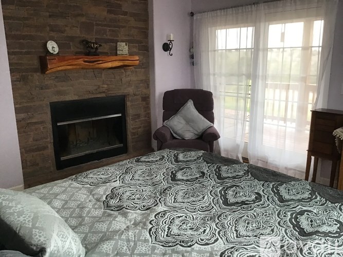 A bedroom with a brick fireplace and a bed with a grey and white patterned comforter.