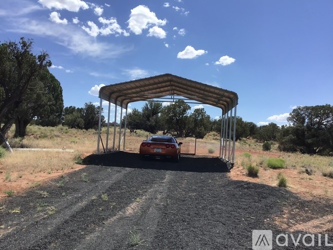 A car is parked under a wooden structure in a rural area.