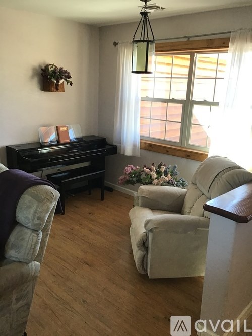 A living room with a piano, two chairs, and a window.