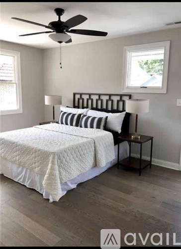 A bedroom with a bed, a ceiling fan, and a small table with a lamp.