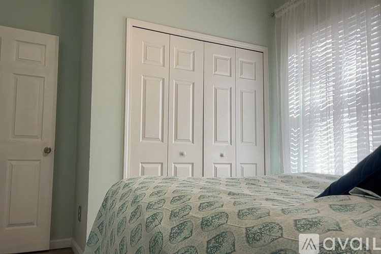 A bedroom with a bed, two doors, and a window with blinds.