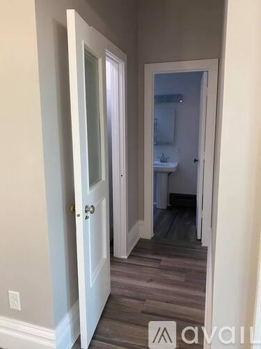 A hallway with a door on the left and a bathroom on the right.