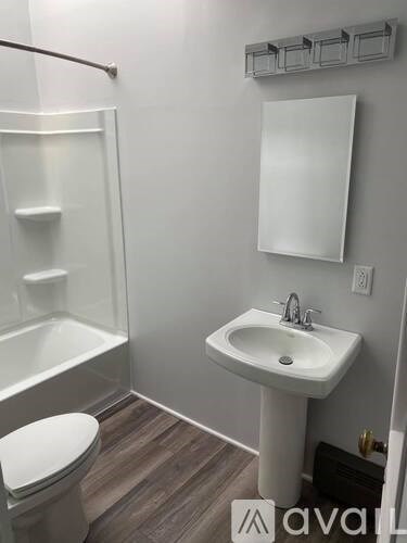 A white sink with a silver faucet is mounted on a white pedestal in a bathroom with a white toilet and a walk-in shower.