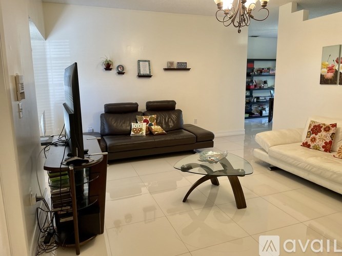 A living room with a brown leather couch, a glass coffee table, and a television.