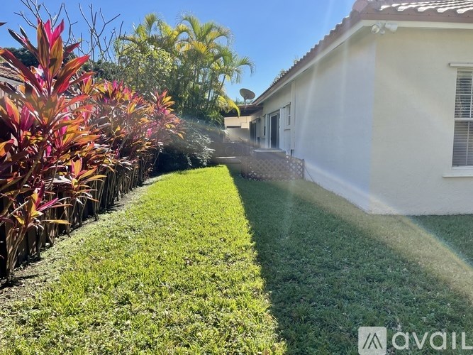 A white house with a well-maintained lawn and a row of red and green plants.