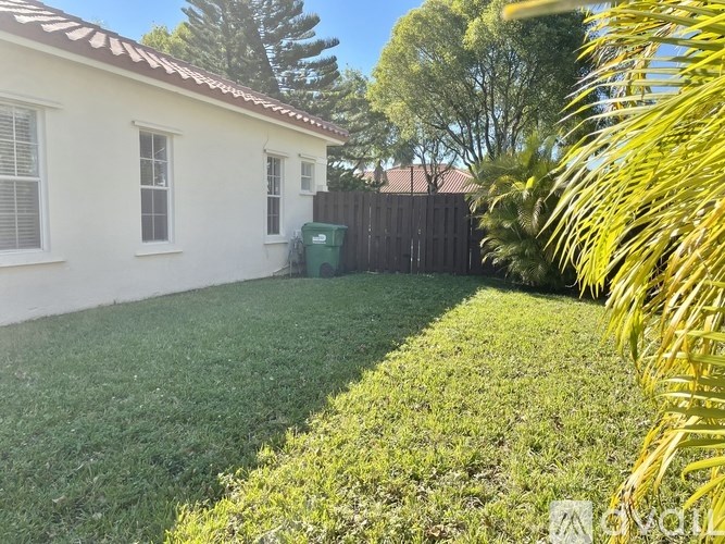 A house with a white exterior and a green trash bin in the yard.