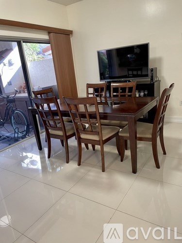 A wooden dining table with chairs in a room with a television.