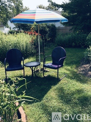 Two chairs and a table are set up under a striped umbrella in a garden.