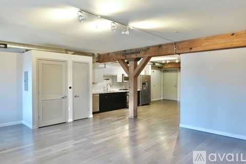A room with wooden floors and a kitchen area in the background.