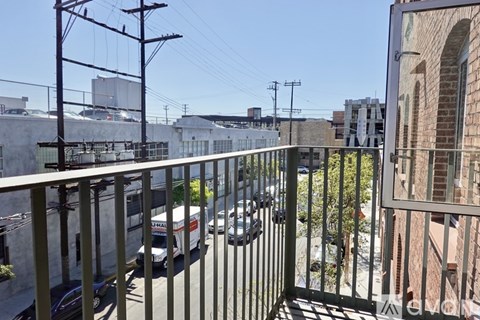 A balcony with a metal railing overlooks a street with cars and buildings.