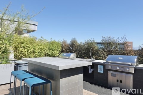 A barbecue grill is on a patio with blue chairs and a table.