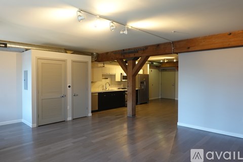 A spacious room with wooden floors and a kitchen area in the background.