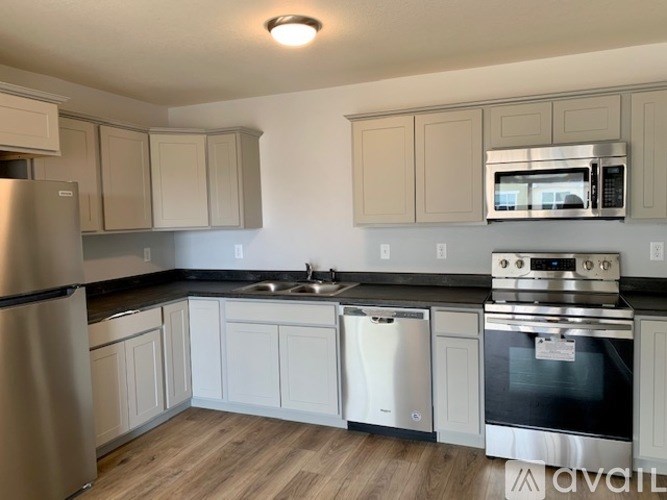 A kitchen with a stainless steel refrigerator, a black countertop, and white cabinets.
