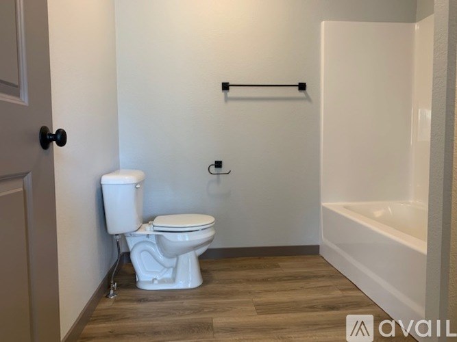 A white toilet in a small bathroom with wood flooring and a white bathtub.