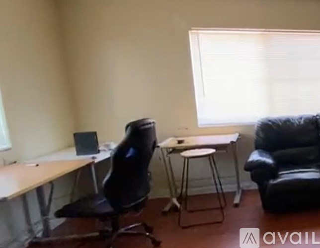 A black office chair is in front of a desk with a laptop and a small table with a stool.