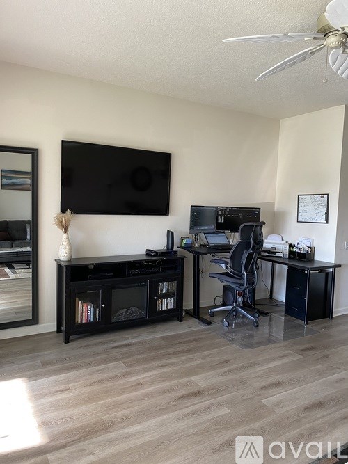 A room with a black TV, a desk with a laptop and a chair, and a fan on the ceiling.