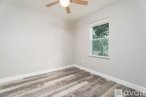 A room with a ceiling fan and a window with a view of trees.