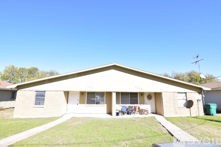 A beige house with a white door and a green trash can in front.