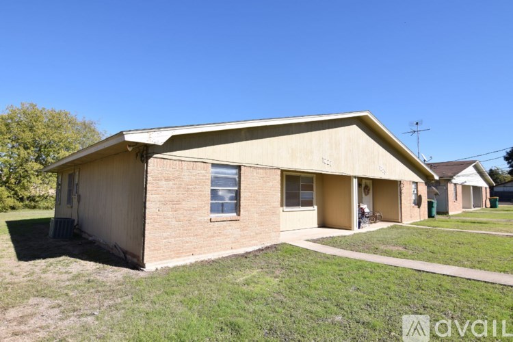 A house with a beige exterior and a brown roof is surrounded by a grassy lawn.