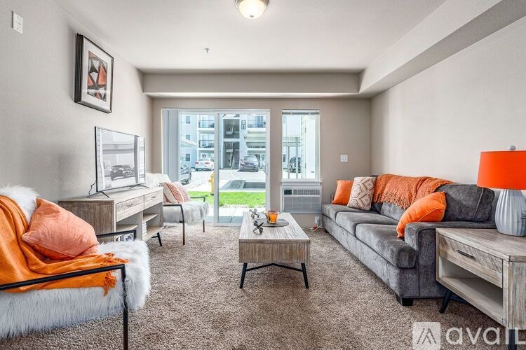 A living room with a grey couch, orange pillows, and a white fur throw.