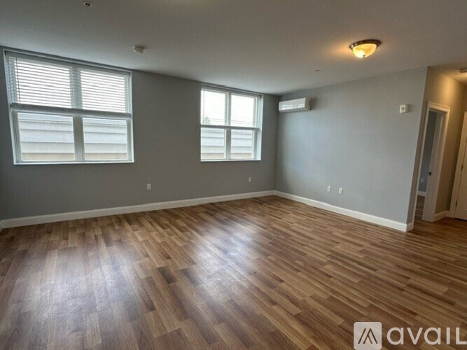 A room with wooden flooring and two windows.