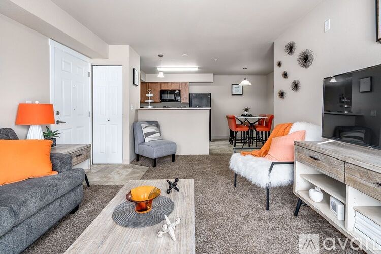 A living room with a grey couch, orange pillow, and a grey rug.