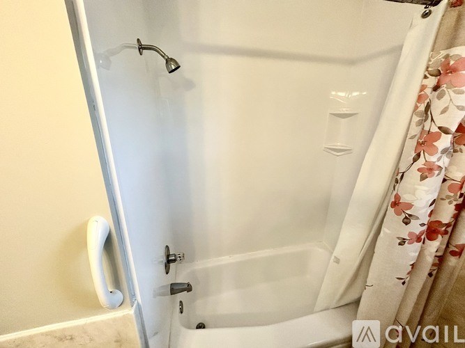 A white bathtub with a shower head and a floral shower curtain.