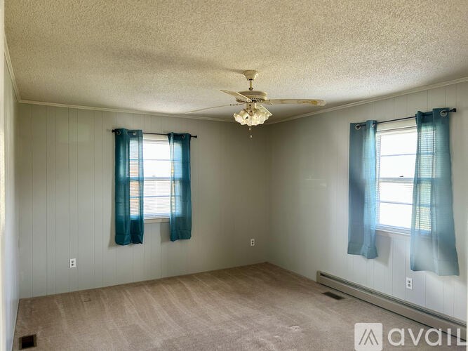A room with a ceiling fan and two windows with blue curtains.