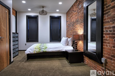 A bedroom with a brick wall and a bed with a white comforter.