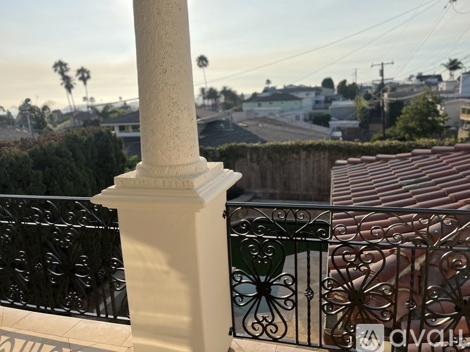 A balcony with a white column and a black wrought iron railing.