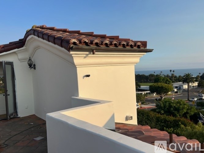 A white building with a red tile roof and a balcony overlooking a street.