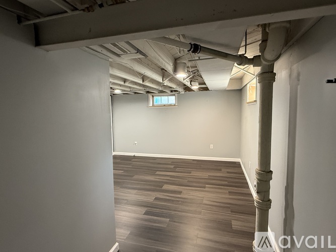 A spacious room with wooden flooring and exposed pipes on the ceiling.