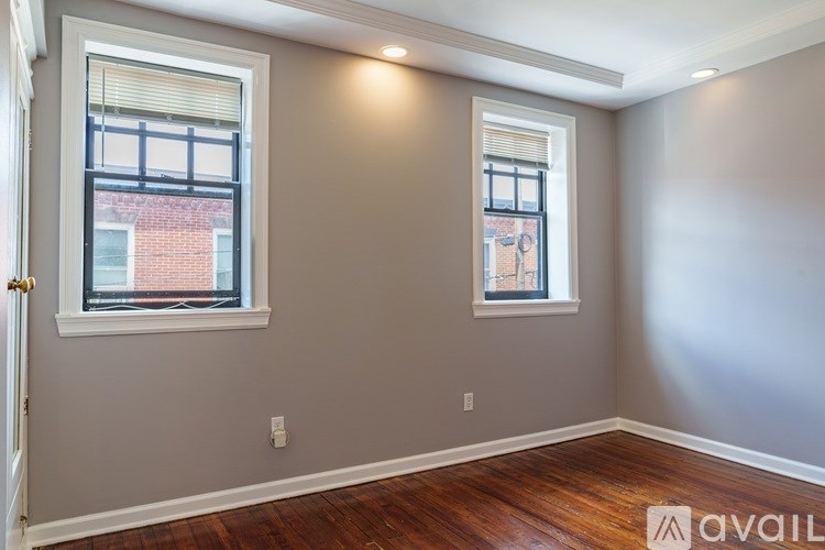A room with two windows and wooden floors is available for rent.