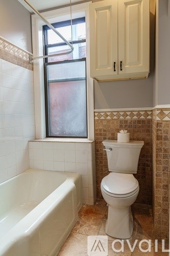 A white toilet is in a bathroom with a white bathtub and a window.
