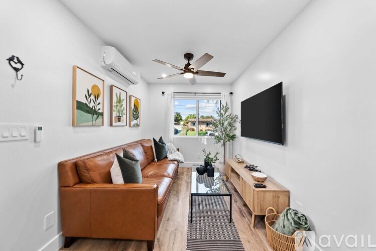 A living room with a brown leather couch, a wooden coffee table, and a flat screen TV mounted on the wall.