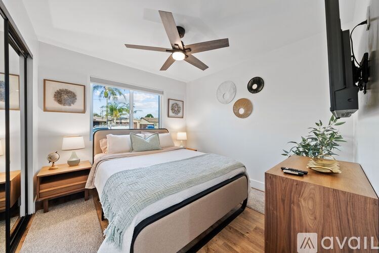 A bedroom with a large bed, a ceiling fan, and a flat-screen TV mounted on the wall.
