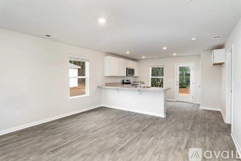 A spacious living room with a kitchen area in the background.
