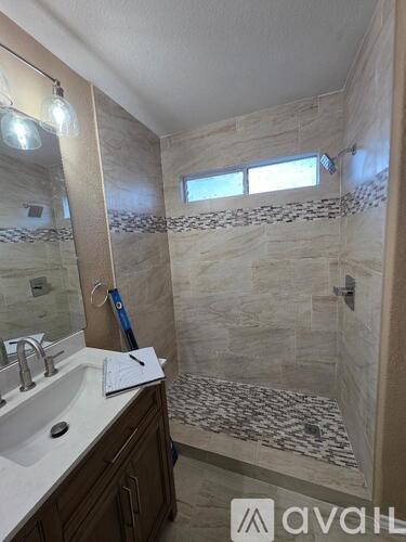 A bathroom with a marble tile shower and a sink with a mirror above it.