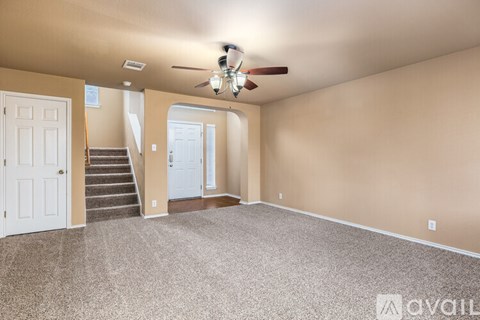 A spacious room with a carpeted floor, a ceiling fan, and a staircase leading to another room.