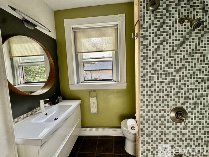 A white sink and toilet paper holder in a green tiled bathroom.
