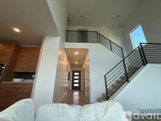 A white couch is in the foreground of a modern interior space with a staircase and wooden cabinets.