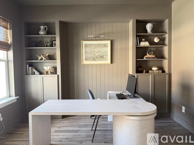 A white desk with a computer on it in a room with shelves and a picture on the wall.