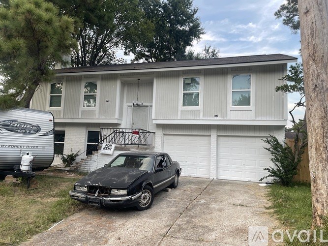 A car is parked in front of a house with a trailer in the background.